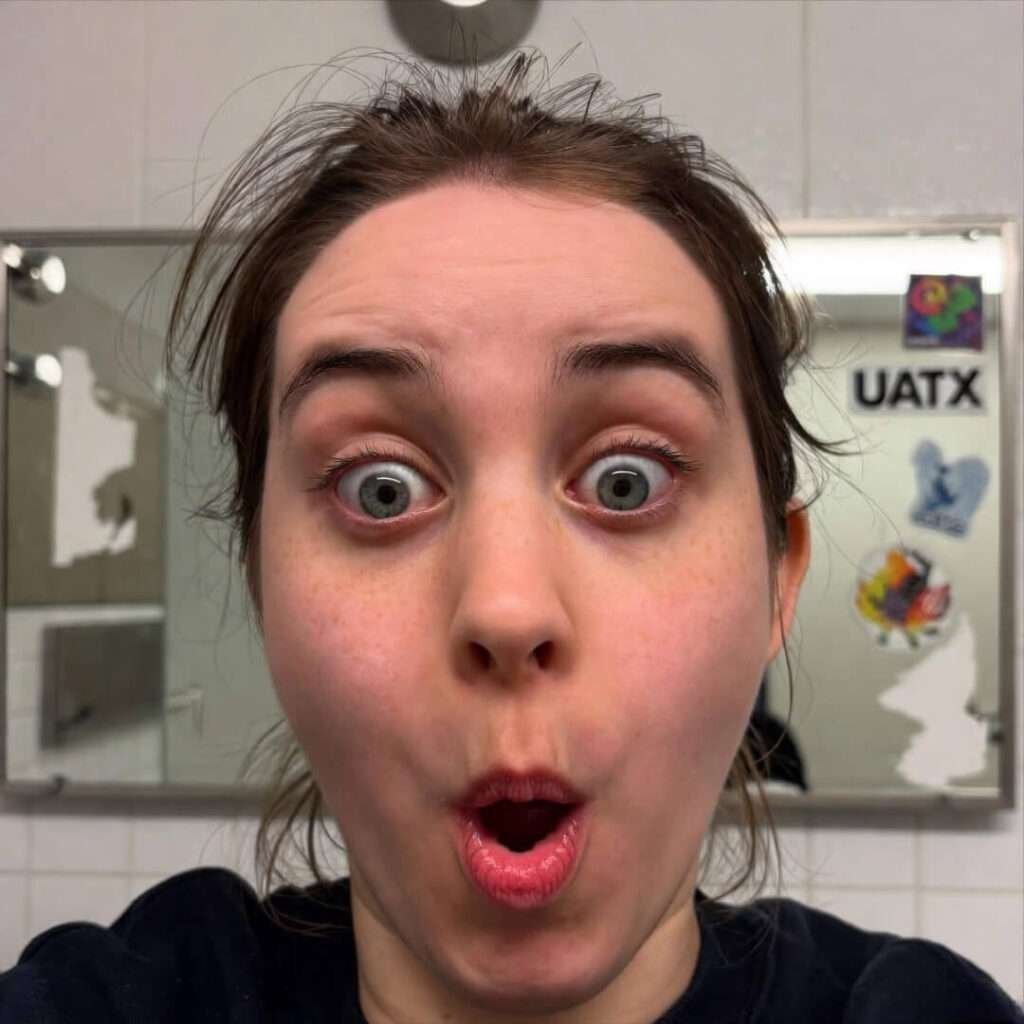 Shocked selfie gesturing at peeling UATX mirror stickers, arm's length fail.