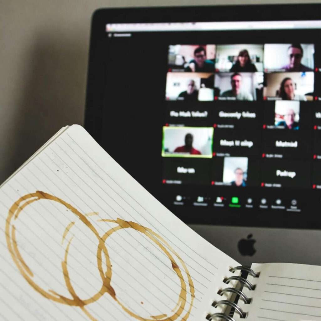 Crumpled notebook with coffee stains beside Zoom screenshot, overhead view.