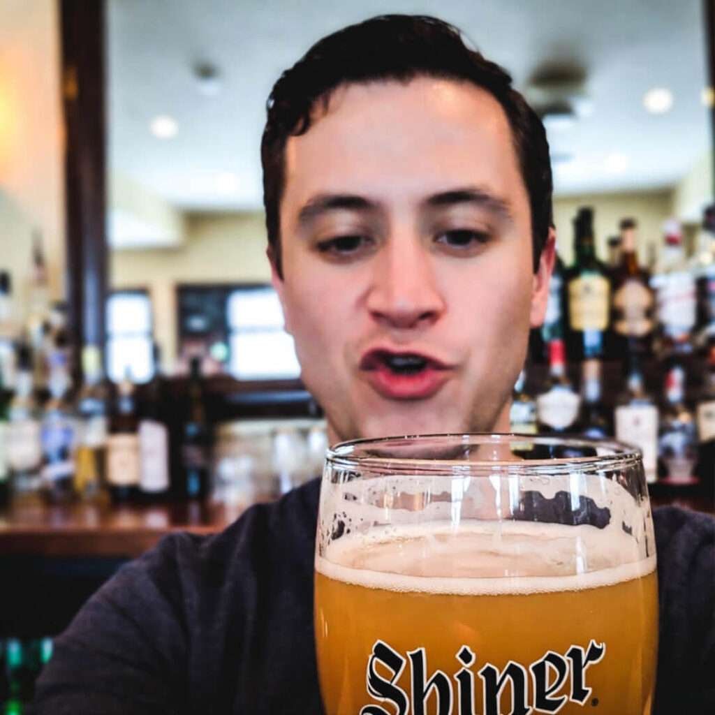 Blurry founder ranting in bar mirror, half-drunk Shiner foreground.